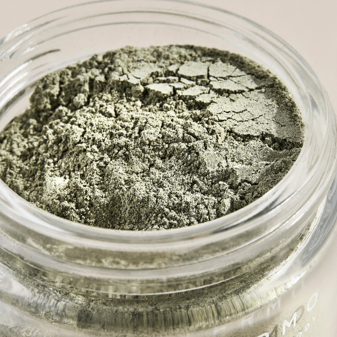 A close-up of a glass jar of Palermo Body Detox Facial Mask shows the fine green powder inside, its surface featuring a cracked texture.