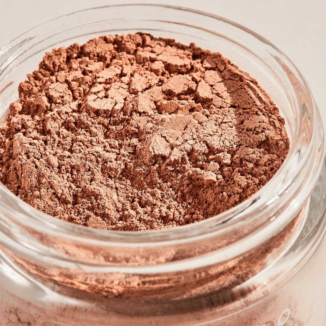 Close-up of a glass jar filled with finely ground, light brown Vitamin C Facial Mask by Palermo Body—perfect for gentle exfoliation and use as a pink clay mask with a textured, cracked surface.