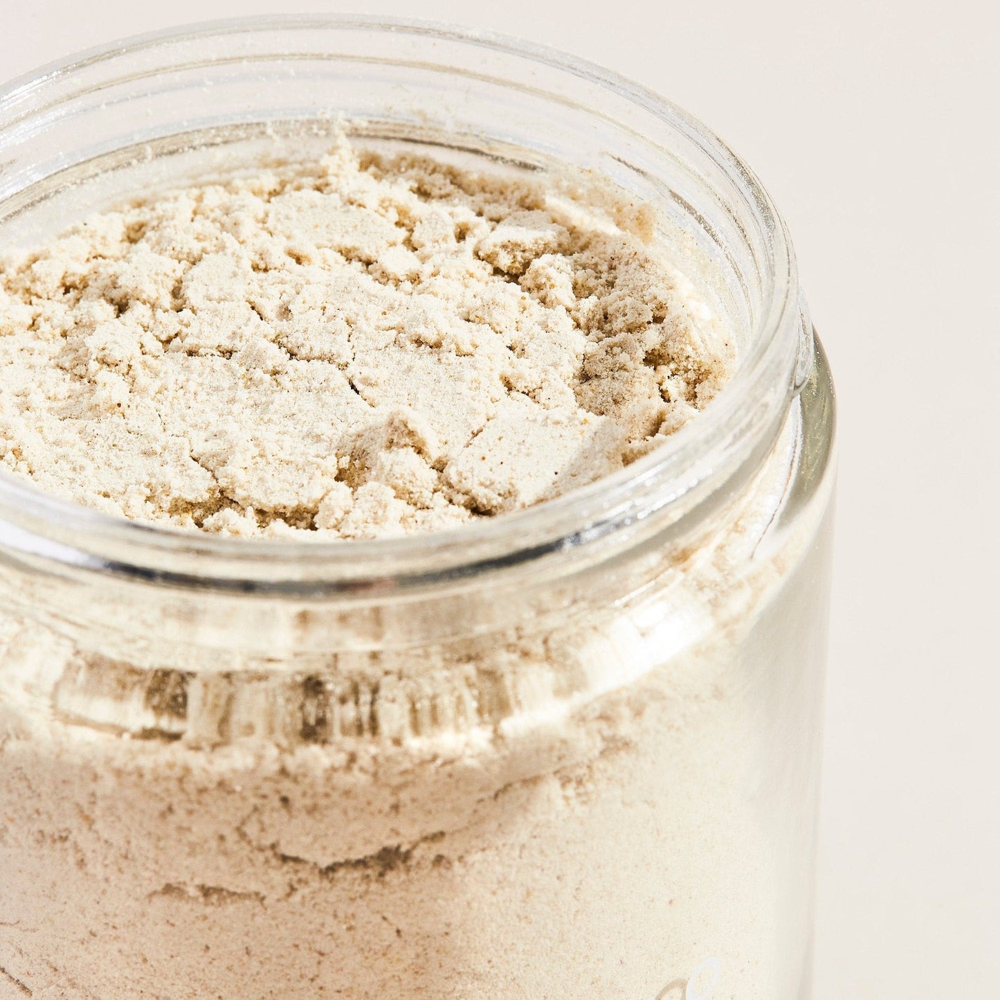 A clear glass jar filled with Palermo Body's Soothing Milk Bath light beige powder is displayed against a plain, light background.