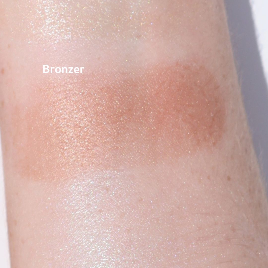 Close-up of a forearm with a swatch of River Organics' Imperfect Highlighters & Bronzers, showcasing a warm, shimmery brown shade in a rectangular patch on the skin labeled "Bronzer.