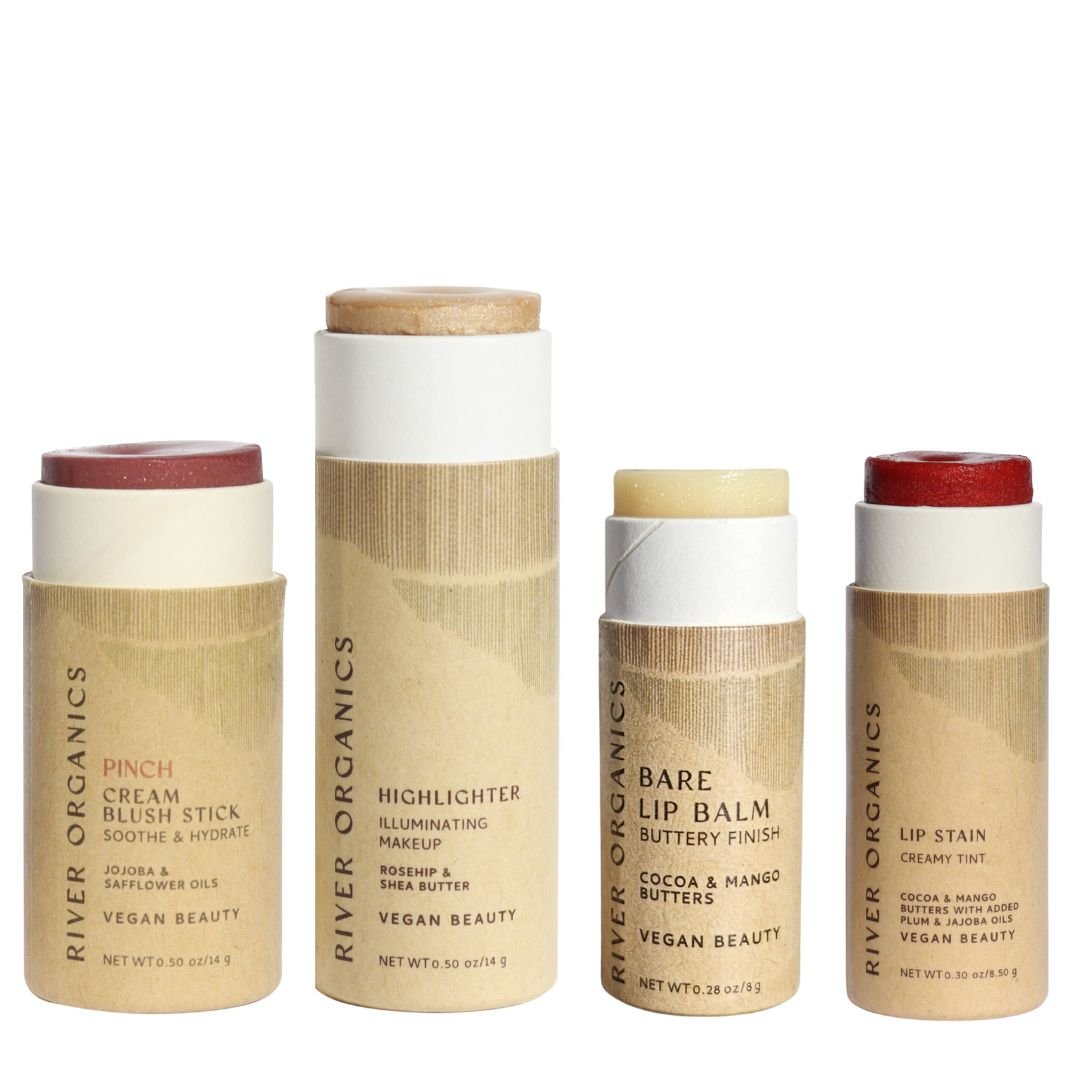 River Organics Colour Sets include four zero-waste vegan makeup sticks—blush, highlighter, lip balm, and lip stain—in eco-friendly cardboard packaging with beige labels.