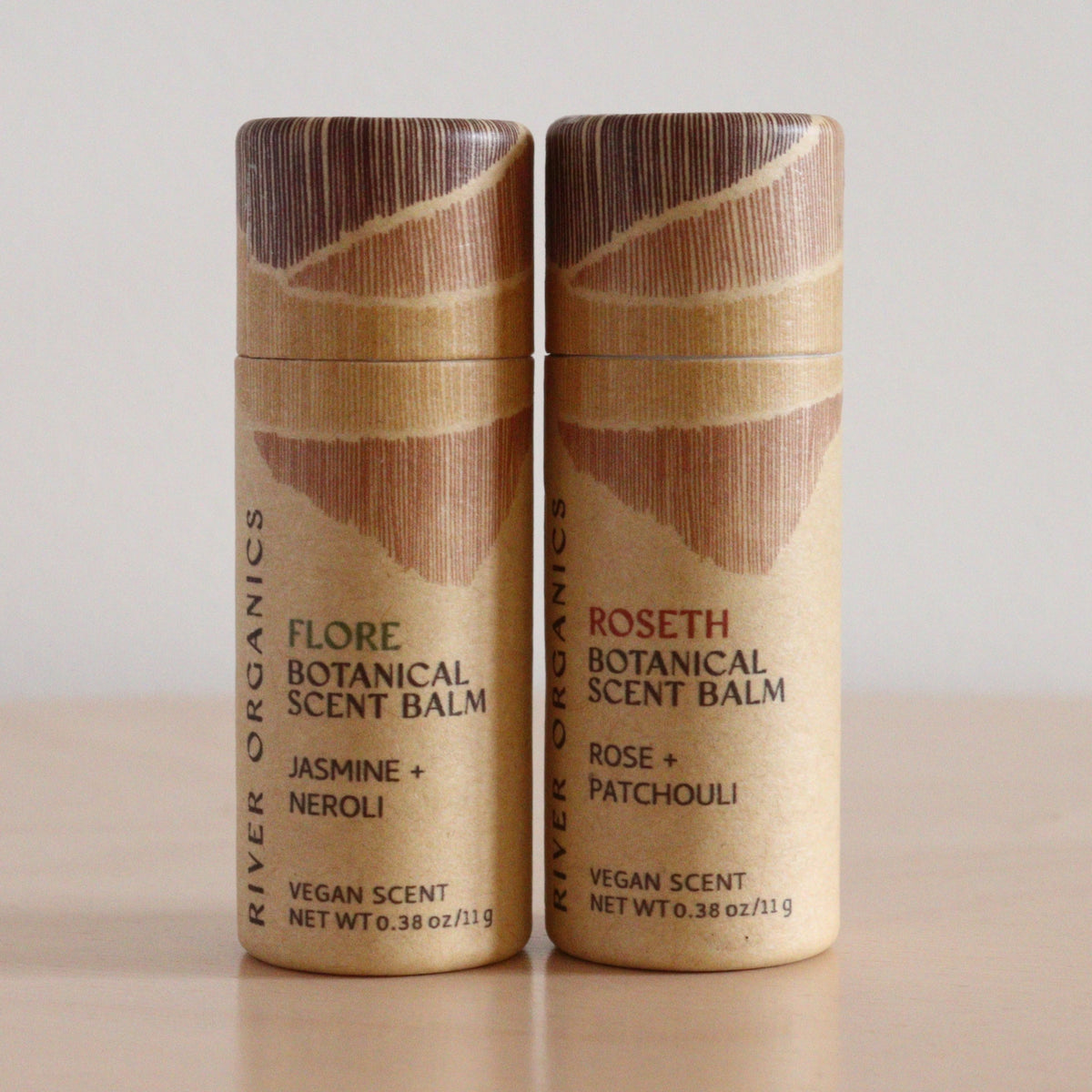 Two River Organics Botanical Scent Balms with essential oils, from the set of 2, stand upright on a light wooden surface. Scents shown: Flore (Jasmine + Neroli) and Roseth (Rose + Patchouli).