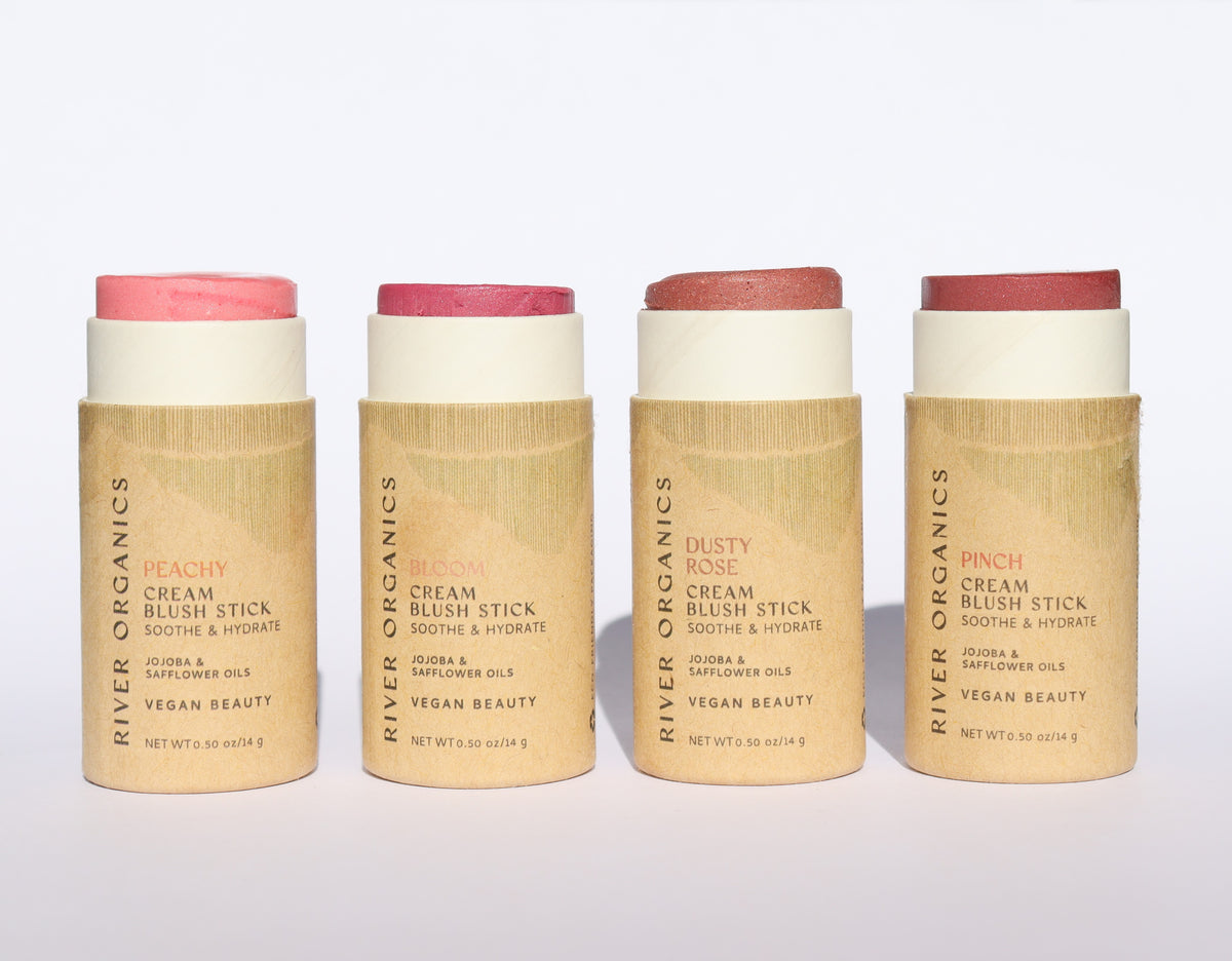 River Organics Brow Wax + Blush + Lip Balm Bundle features vegan blush sticks in Peachy, Bloom, Dusty Rose, and Pinch. Housed in cardboard tubes, each shade lists its name and product details—perfect for lips and cheeks.