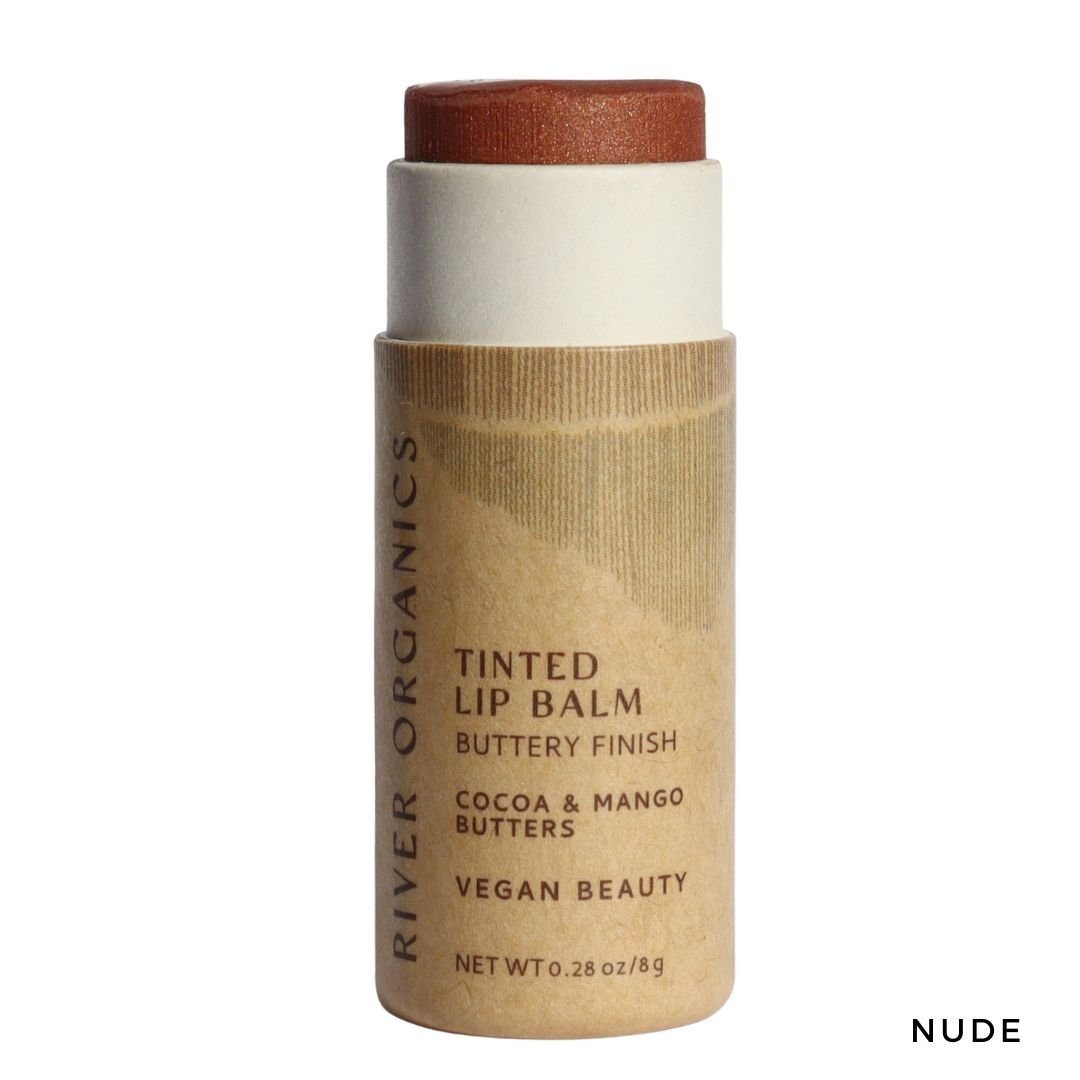 River Organics Tinted Vegan Lip Balm in “Nude” features a reddish-brown stick, brown paper label, and is made with plant-based ingredients like cocoa and mango butters for deep moisture and a buttery, vegan finish.