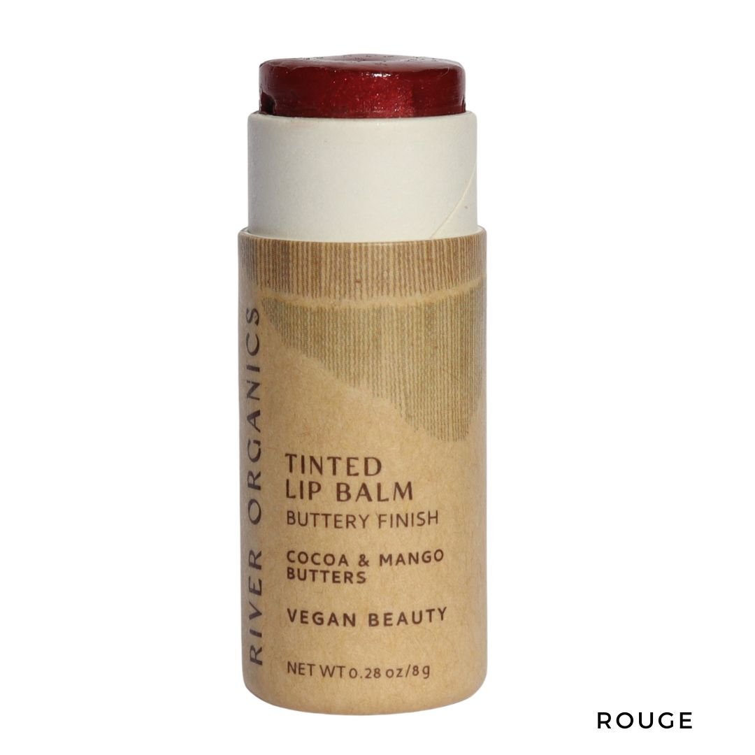 A tube of River Organics Tinted Vegan Lip Balm in "Rouge" with red balm exposed. The label notes a buttery finish, cocoa & mango butters, deep moisture, plant-based ingredients, vegan beauty. Net wt 0.28 oz.