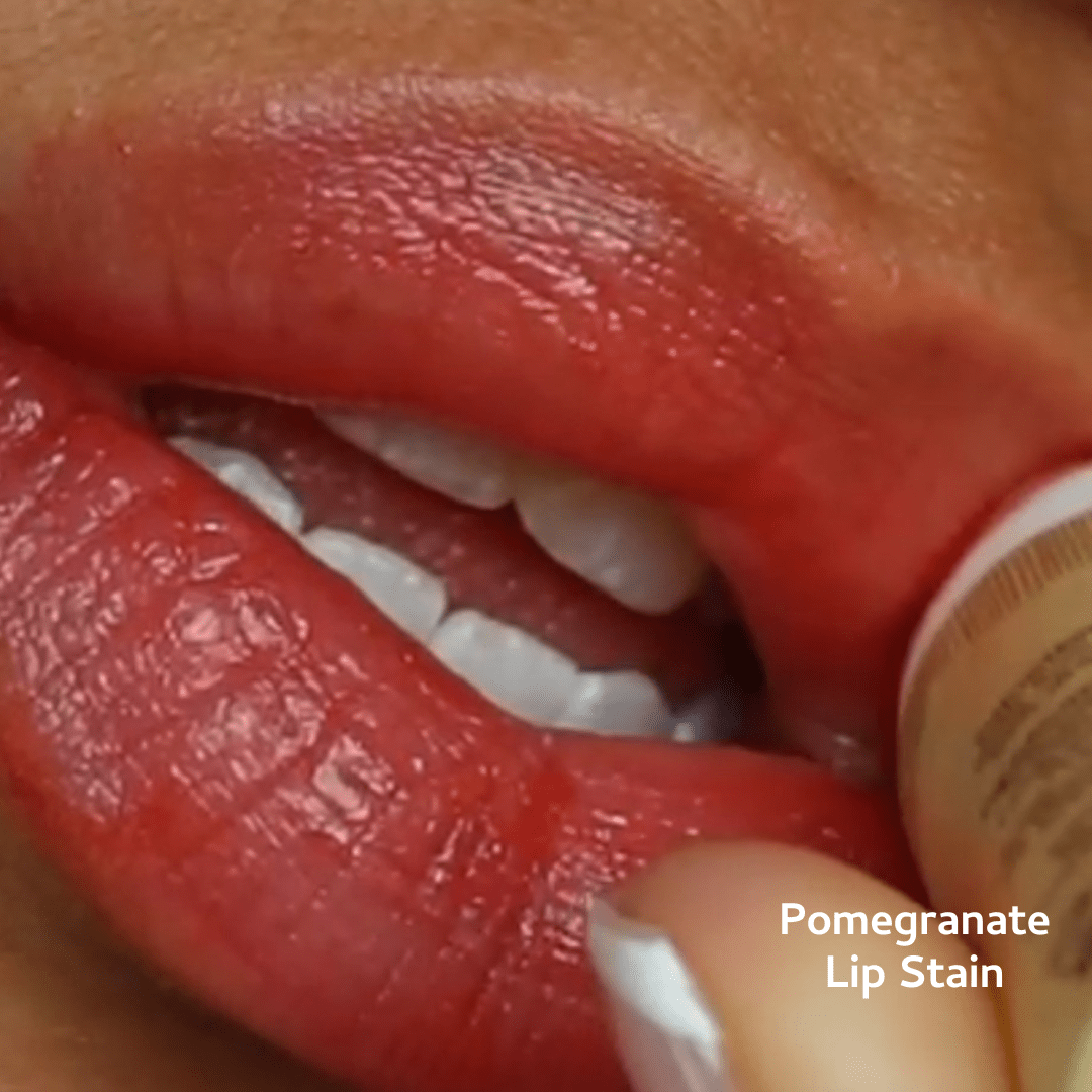 Close-up of lips tinted with a red, plastic-free Vegan Lip Stain by River Organics, as a hand holds the tube; "Vegan Lip Stains" appears in the bottom right corner.