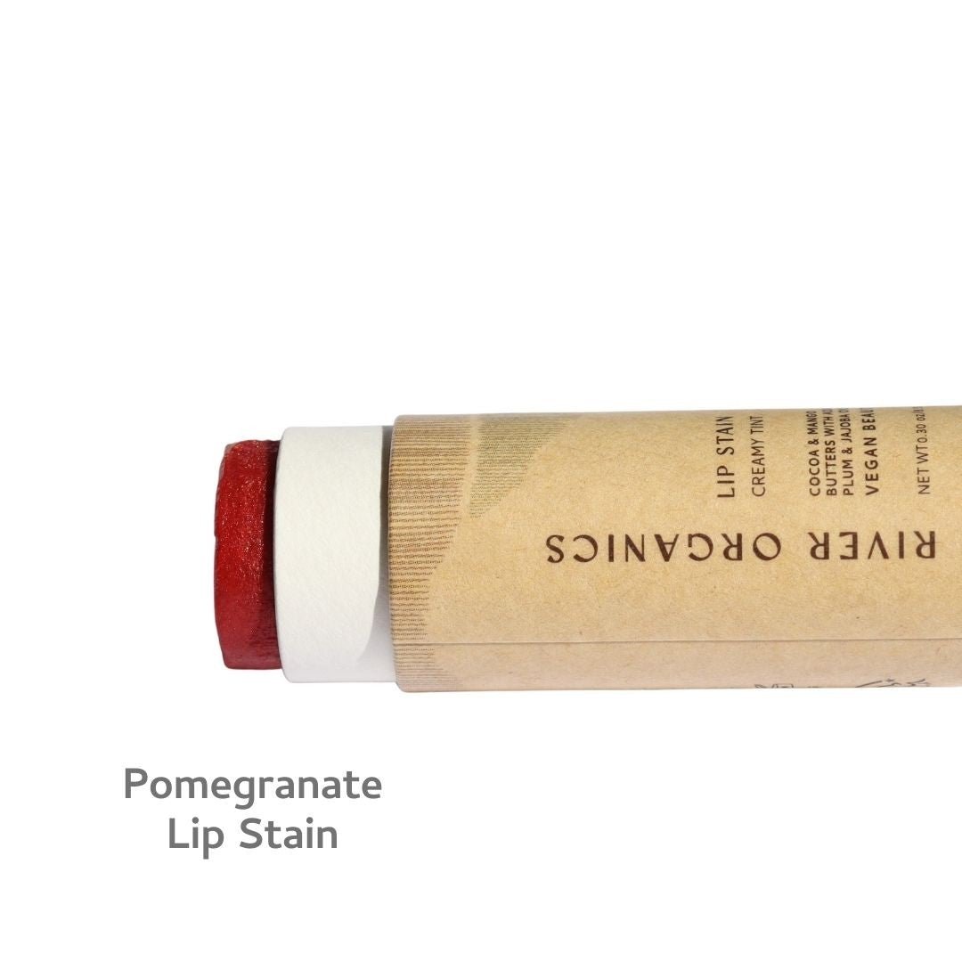 A brown cardboard tube labeled "River Organics" lies horizontally, revealing a deep red vegan lip stain. Text below reads "Vegan Lip Stains" on a white background.
