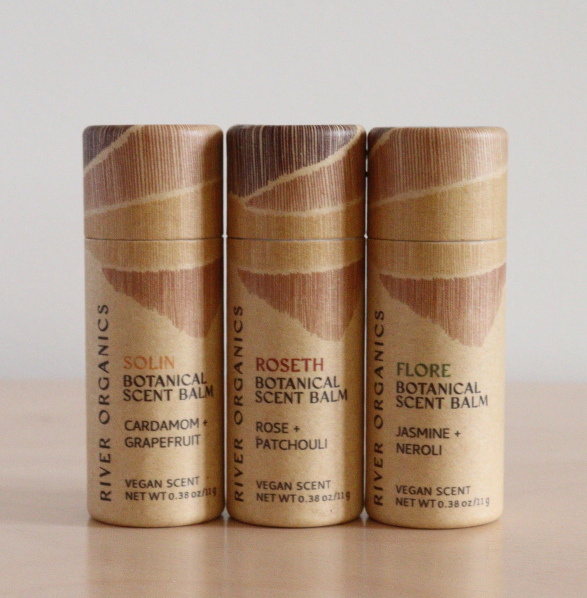 A set of three River Organics Botanical Scent Balms with essential oils—Solin (Cardamom + Grapefruit), Roseth (Rose + Patchouli), and Flore (Jasmine + Neroli)—stand upright in natural cylindrical packaging on a light surface.