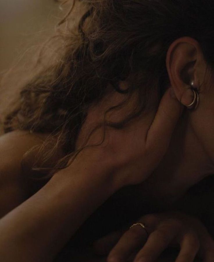 Close-up of a person with curly hair lying down, wearing hoop earrings and a ring, in soft warm light—evoking the calming ambiance of River Organics' Roseth: Rose + Patchouli Botanical Scent Balm.