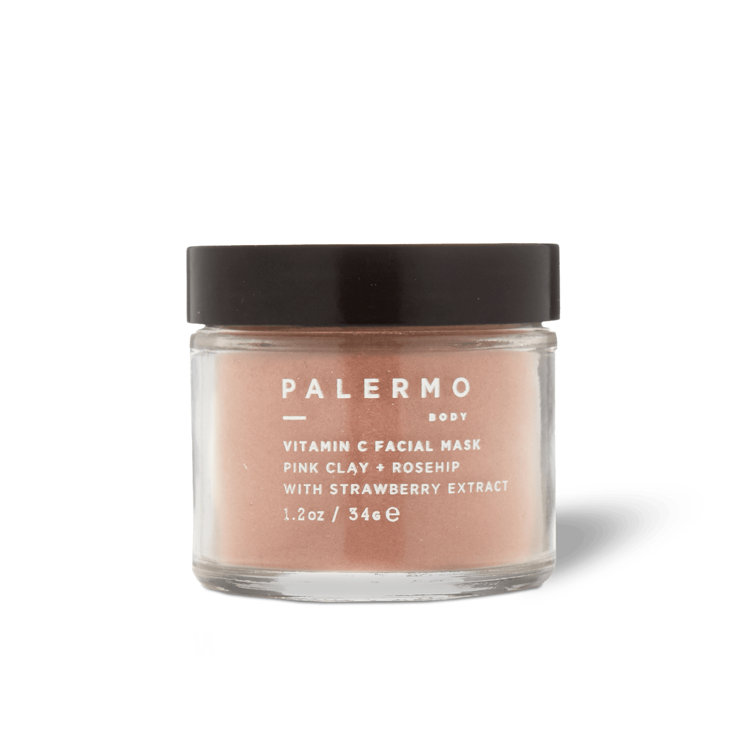 A clear glass jar with a black lid holds Palermo Body's Vitamin C Facial Mask, made with pink clay, rosehip, and strawberry extract for gentle exfoliation. The front label displays white text.