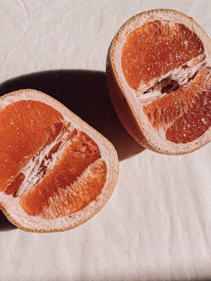 Two halves of a pink grapefruit with light rind rest on a textured white surface, evoking the fresh notes in River Organics' Botanical Scent Balms - Stick solid perfumes made with nourishing plant oils.