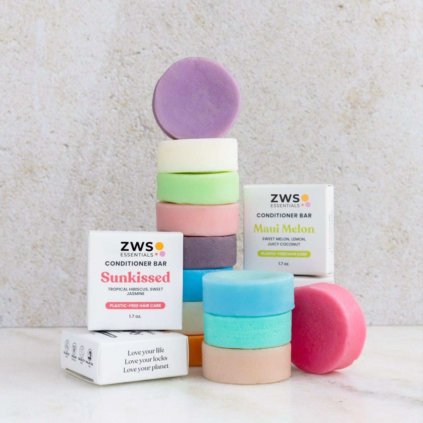 Colorful round Conditioner Bars from ZeroWasteStore.com in "Sunkissed" and "Maui Melon" scents are stacked near two branded boxes on a light surface. These vegan, eco-friendly hair care bars offer a zero waste alternative.