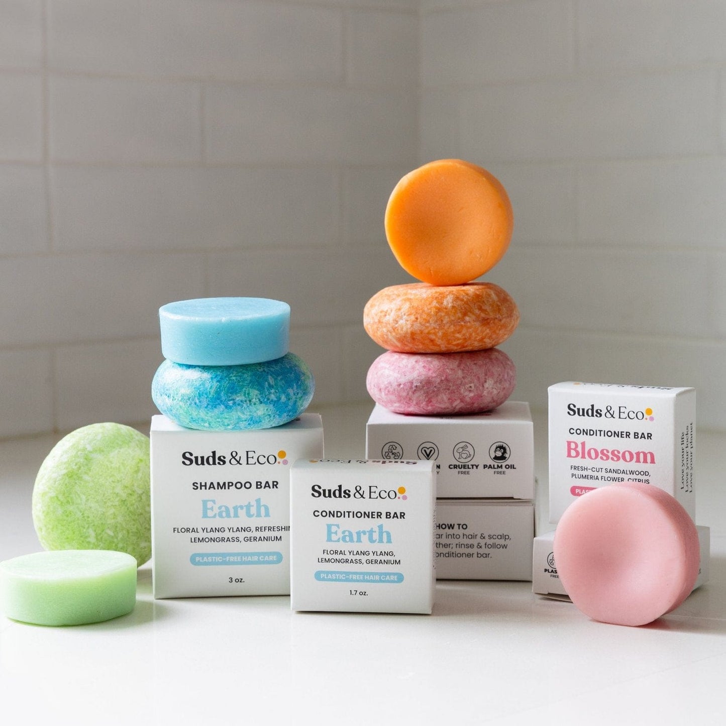 Colorful Conditioner Bars from ZeroWasteStore.com are stacked with branded boxes on a white surface against a white tile background—highlighting vegan, zero waste haircare for an eco-friendly routine.