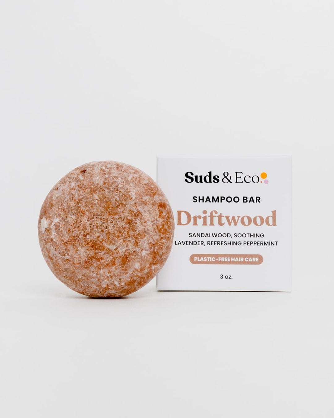A round, brownish SLS-free Shampoo Bar from ZeroWasteStore.com sits before a box labeled "Shampoo Bar Driftwood," highlighting sandalwood, lavender, peppermint, and promoting plastic-free, zero-waste hair care.