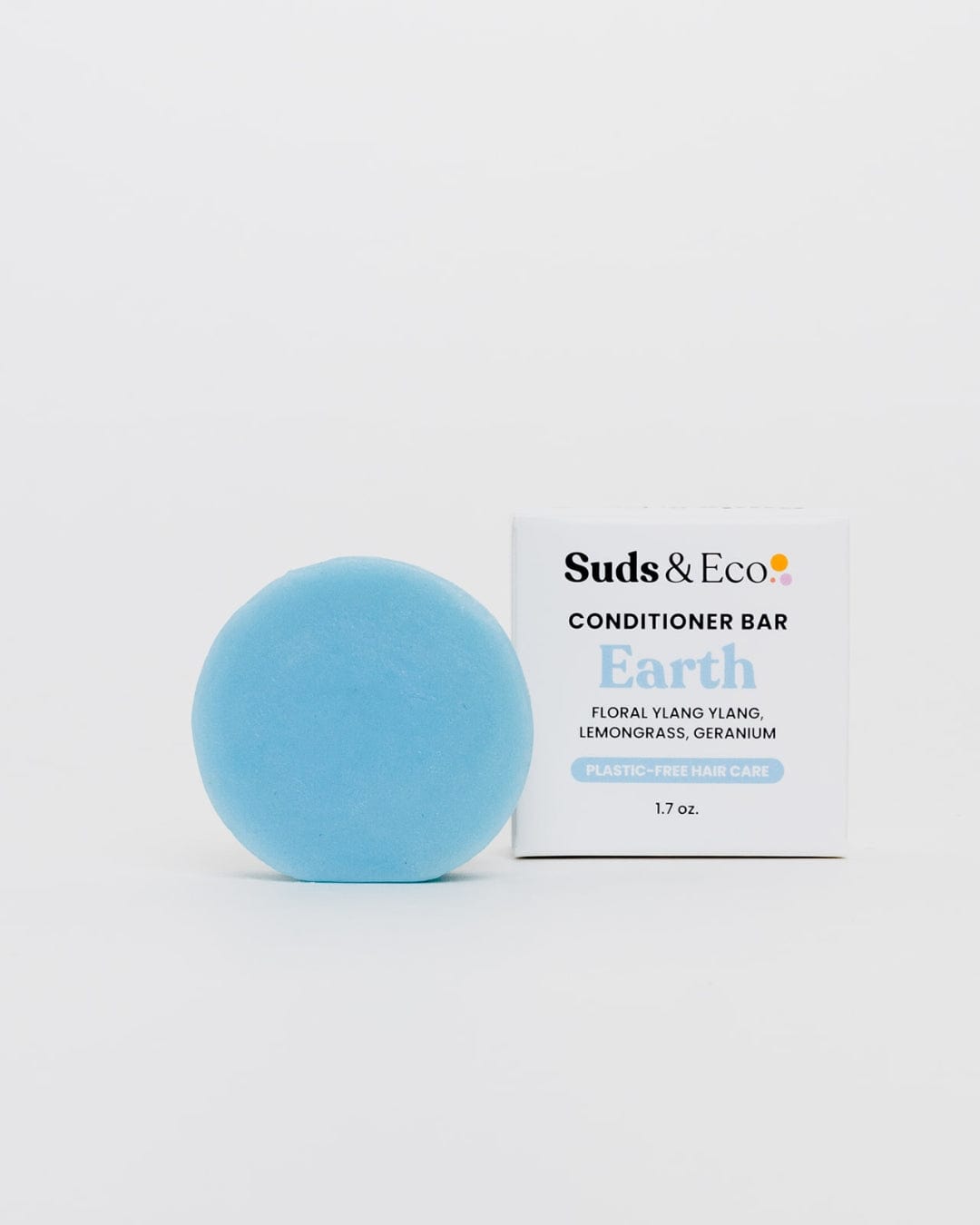 A round, light blue vegan Conditioner Bar from ZeroWasteStore.com sits by a white box with ylang ylang, lemongrass, and geranium for zero waste, plastic-free hair care.