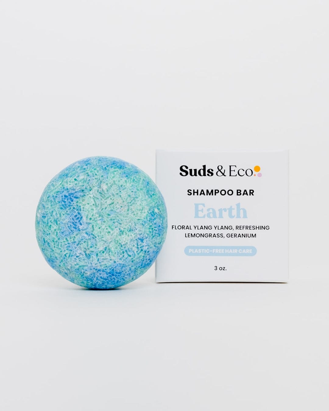 A blue and green round vegan Shampoo Bar by ZeroWasteStore.com sits beside a white box labeled “Shampoo Bar Earth” with ylang ylang, lemongrass, and geranium scents—SLS free, plastic-free hair care.