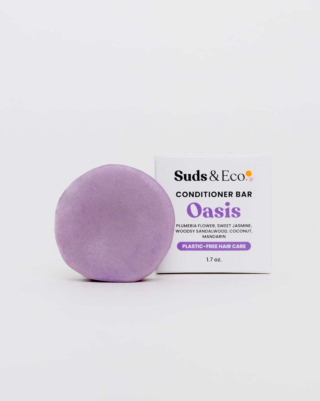 A round, purple Conditioner Bar from ZeroWasteStore.com sits by its box labeled "Conditioner Bar," featuring plumeria, jasmine, coconut, woodsy, and mandarin notes. The packaging highlights plastic-free hair care and zero waste benefits.