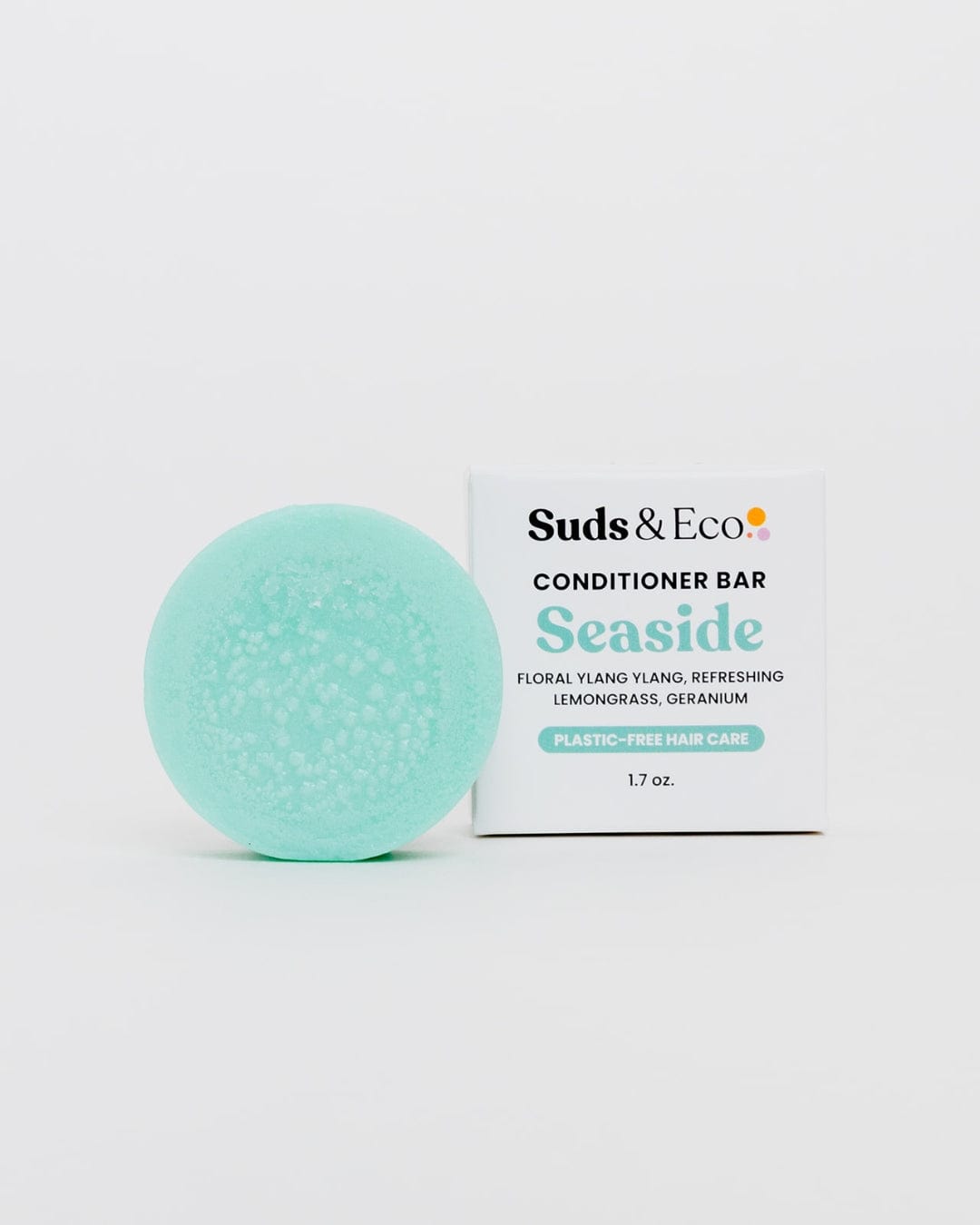A turquoise round Conditioner Bar from ZeroWasteStore.com sits beside its white box, offering refreshing lemongrass and geranium scents for vegan, plastic-free hair care.