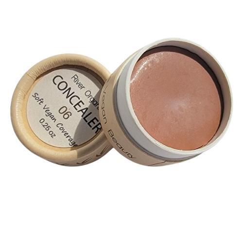 A small, round container of River Organics Zero-Waste Vegan Concealer 06 with light brown cream inside. The partially open lid displays the label: "Soft Vegan Coverage, 0.25 oz." This natural, hydrating concealer offers effortless zero-waste beauty.