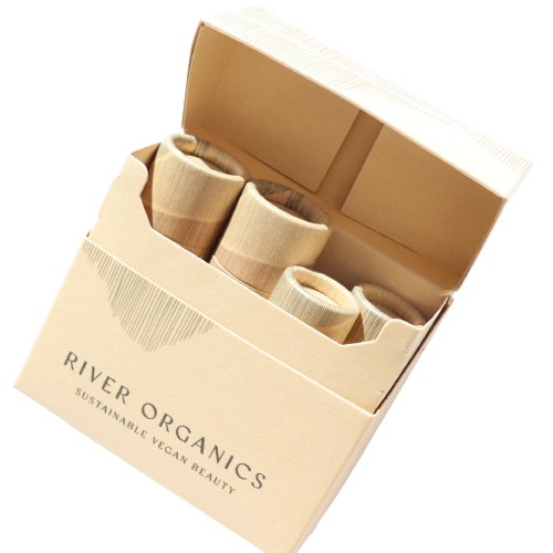 The "Gift Box" by River Organics is an open cardboard box containing paper-wrapped cylindrical objects, labeled with "River Organics Sustainable Vegan Beauty," offering a perfect, elegant combination for eco-conscious beauty enthusiasts.