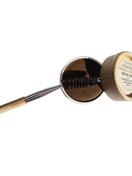 A jar of Jojoba Grooming Lip with its lid removed reveals a brown cosmetic product. Resting on the jar is River Organics' Eco-Friendly Double-Sided Bare Wood Brow & Mascara Brush, angled left like a mascara wand against a white background.