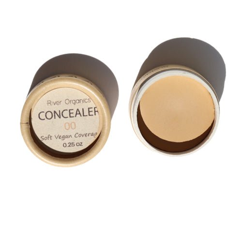 Two small, round containers of River Organics Sample Size | Zero Waste Concealer, shade 00, are shown. One container is open, revealing the light beige concealer with buildable coverage, while the other is closed with the label visible, reading "River Organics Sample Size | Zero Waste Concealer 00 Soft Vegan Coverage 0.25 oz.