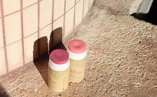 Two zero-waste multi-function creamy blush sticks in Peachy and Bloom colors, with caps off against a pink tiled column