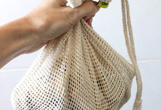 A hand holding a produce bag containing zero-waste cosmetics