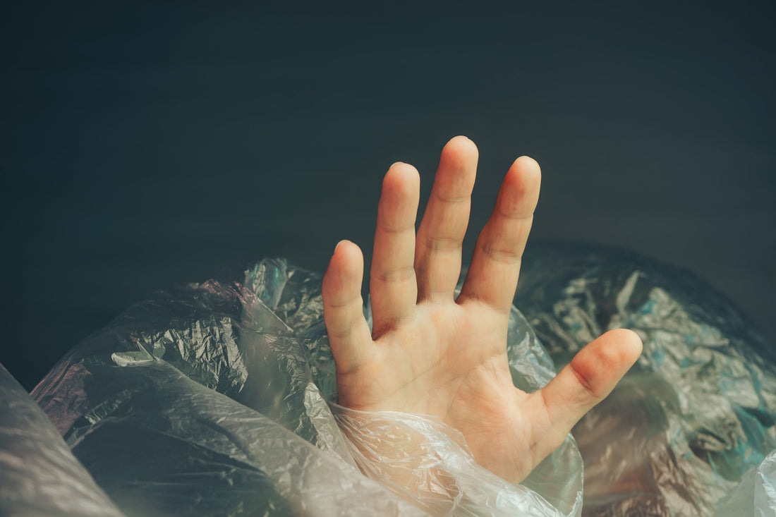 a hand reaches out through a bunch of plastic waste as if drowning