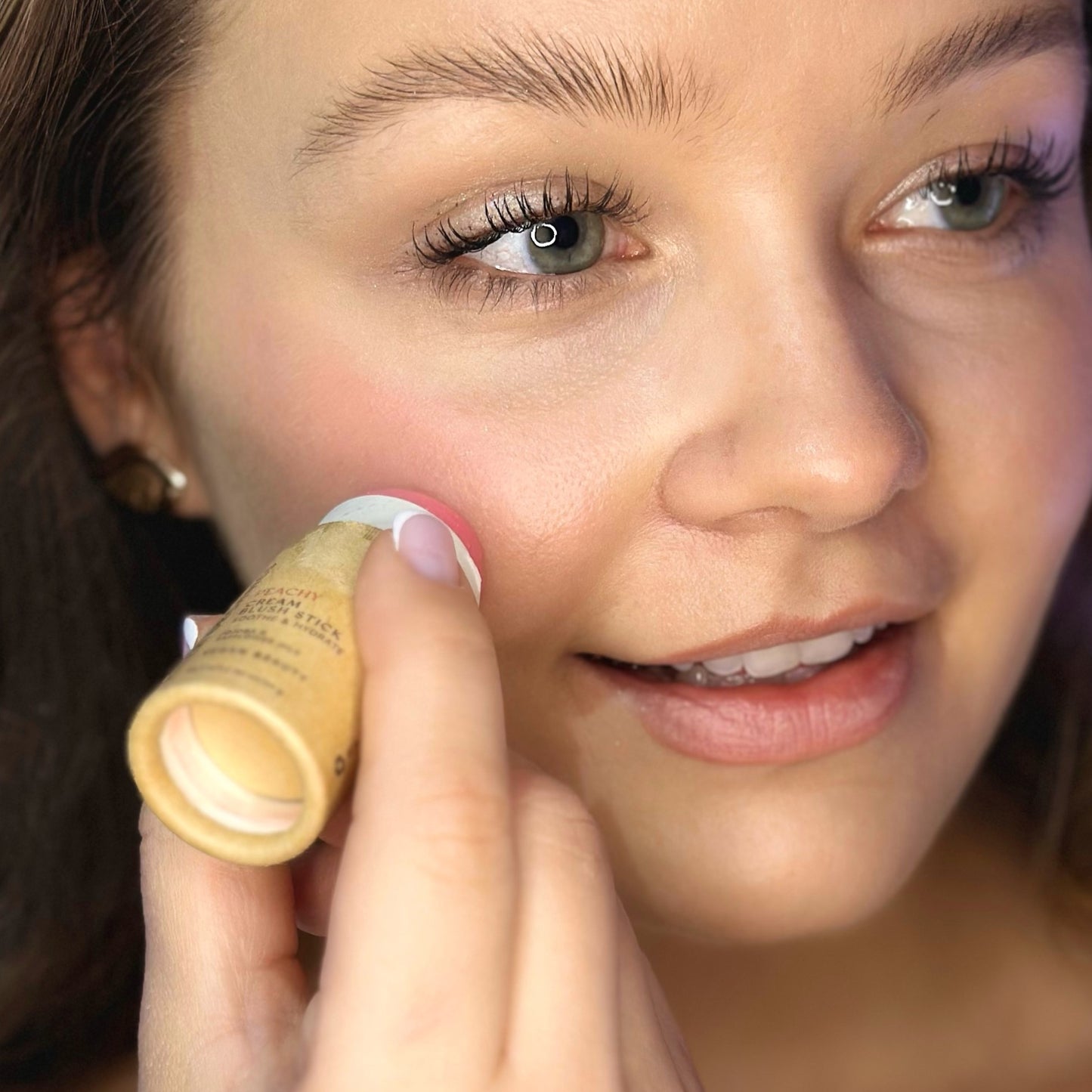 Model swiping Creamy Vegan Blush Stick in Peachy onto cheeks.