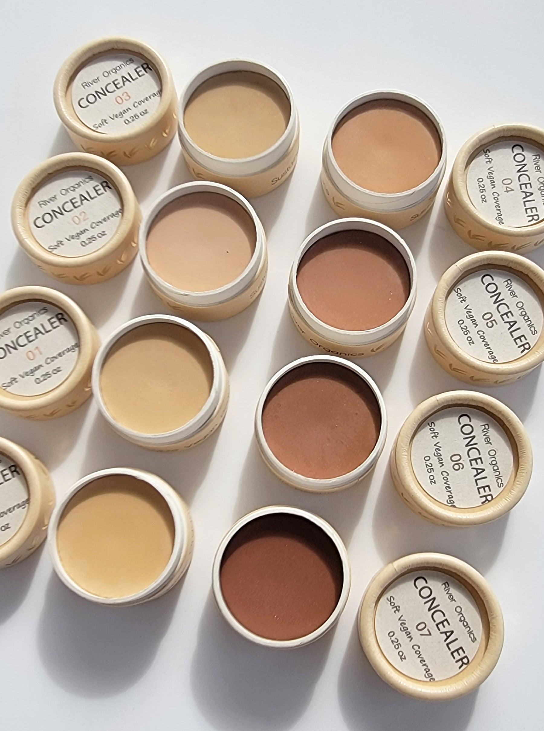 Open jars of River Organics Conceal & Brow Duo - Zero-Waste Vegan Beauty Set, labeled by shade, are neatly arranged on a white surface to display a range of tones from light to dark—showcasing this eco-friendly beauty option.