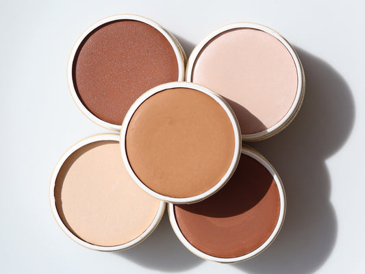 Five open River Organics foundation containers in assorted shades, including the Zero-Waste Vegan Concealer (Titanium Dioxide-Free), are arranged closely in a flower-like formation against a white background.