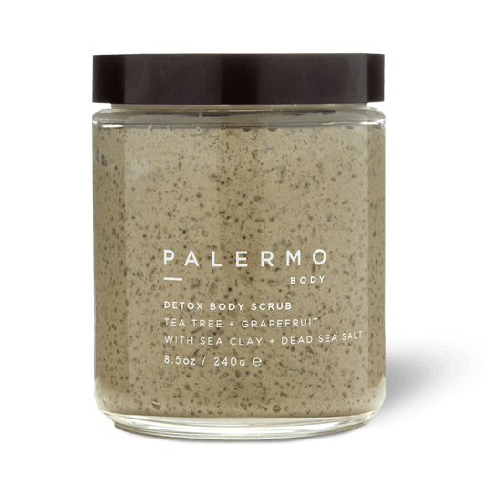 Palermo Body's Detox Body Scrub comes in a clear glass jar with a black lid. The label highlights Dead Sea salt, sea clay, tea tree, and grapefruit. Inside is a beige scrub with visible speckles for an invigorating cleanse.