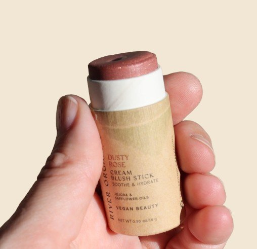 A hand holds the Creamy Vegan Blush stick in Dusty Rose showing stick color.