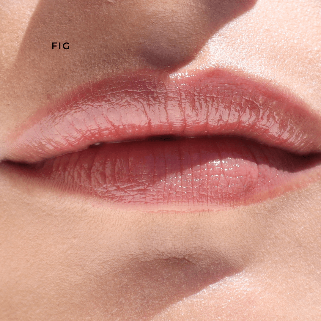 A close-up showcases natural, glossy lips with a soft pink hue from River Organics' Vegan Lip Stains. The smooth skin contrasts with the word "FIG" to the upper left, symbolizing sustainable beauty.