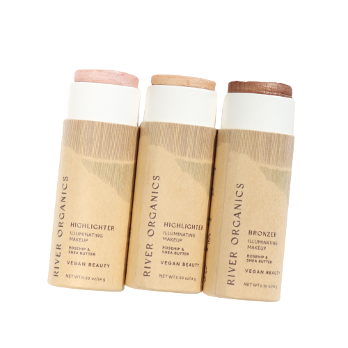 Three wooden tubes of River Organics Skincare Highlighter and Bronzer Sets are pictured against a white background. From left to right: a pink highlighter, a golden highlighter, and a bronzer. Each tube is labeled with details about the product's nature and ingredients.