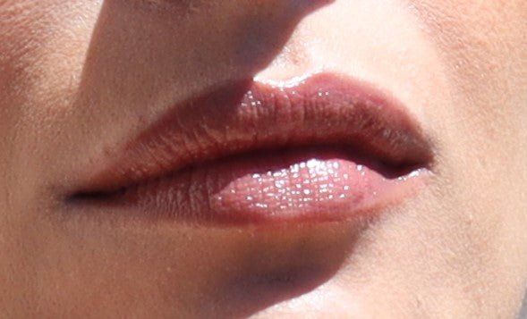 Close-up of a person's lips, slightly parted with a glossy sheen from River Organics Fig Vegan Lip Stain. The skin texture around the lips is visible in the well-lit image. No other facial features or accessories are shown.