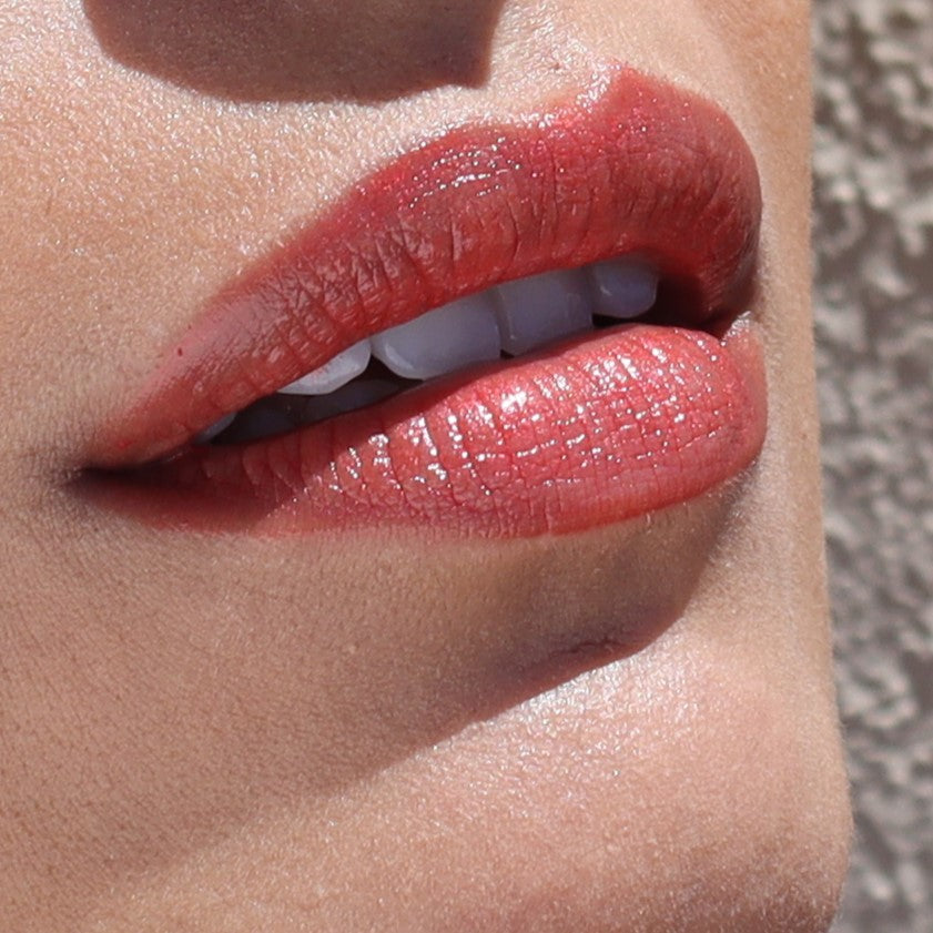 Close-up of lips wearing River Organics Vegan Lip Stain in a natural shade, showing white teeth. The skin is smooth and background blurred. This plastic-free, organic lip stain offers long-lasting color in all shades.