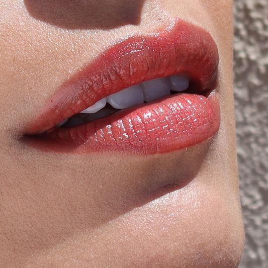 Close-up of lips wearing River Organics Vegan Lip Stain in a natural shade, showing white teeth. The skin is smooth and background blurred. This plastic-free, organic lip stain offers long-lasting color in all shades.