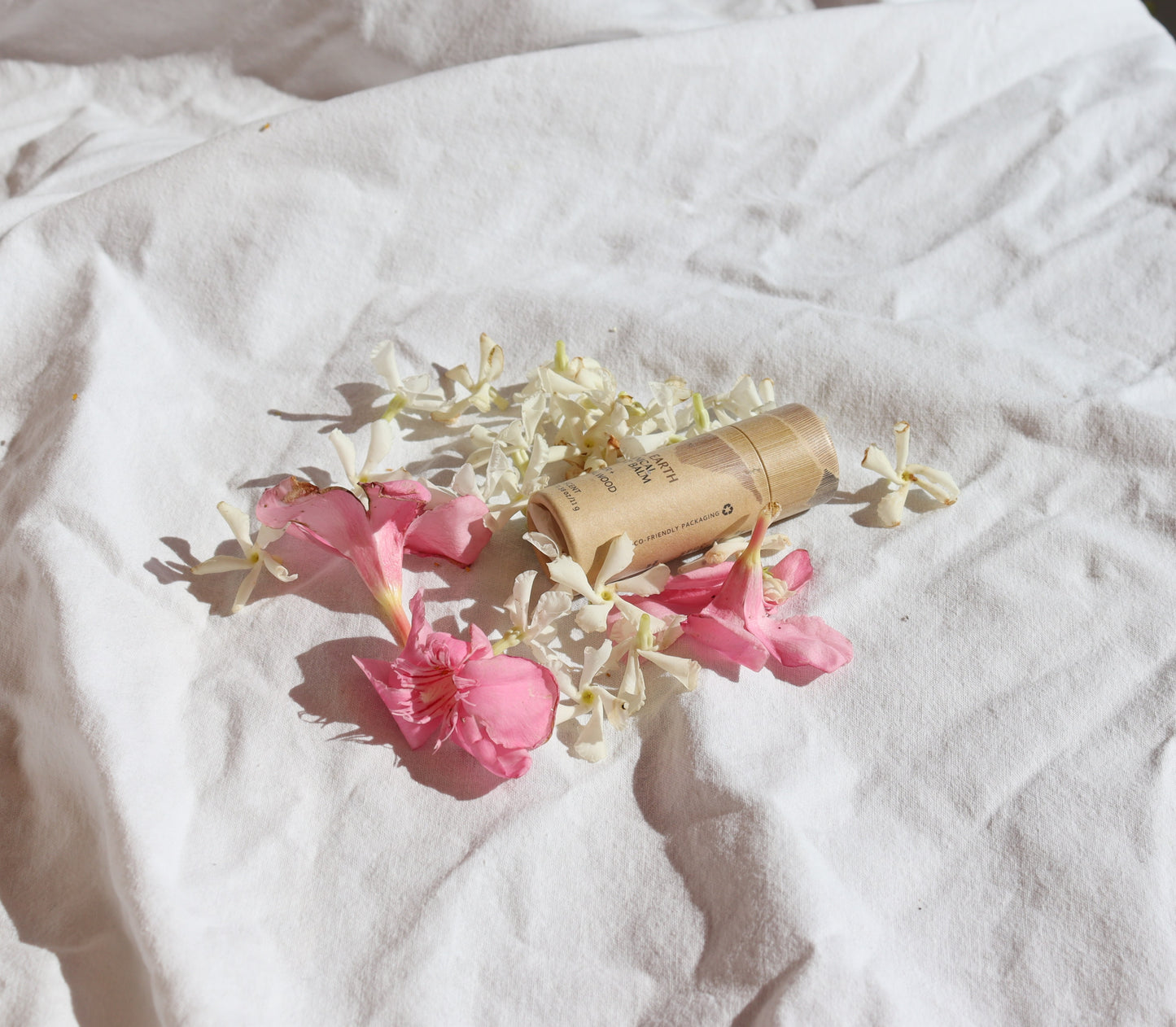 A set of 2, 3, or 4 Botanical Scent Balms by River Organics, made with essential oils, lies on soft white fabric in bright natural light, surrounded by scattered white and pink flower petals.