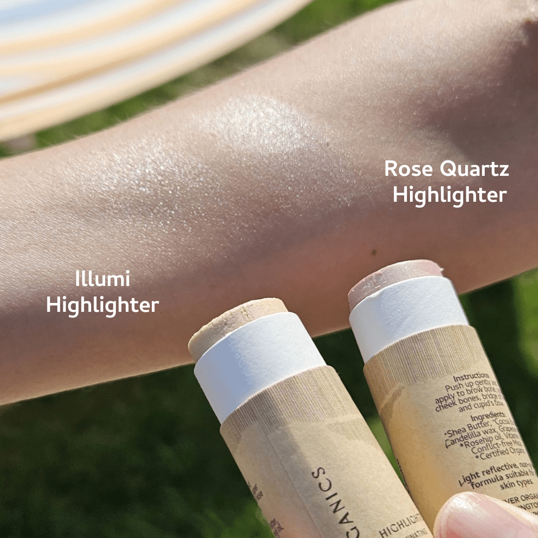 Two arms demonstrate the River Organics Rose Quartz Vegan Highlighter Stick in soft pink and Illumi Highlighter in light beige, both enriched with organic botanicals. They provide natural radiance and subtle shimmer on the skin, set against a vibrant outdoor backdrop.