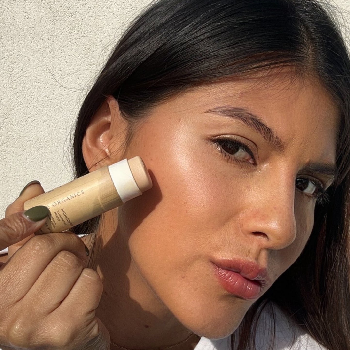 An olive skin toned girl demonstrates illumi highlighter stick 