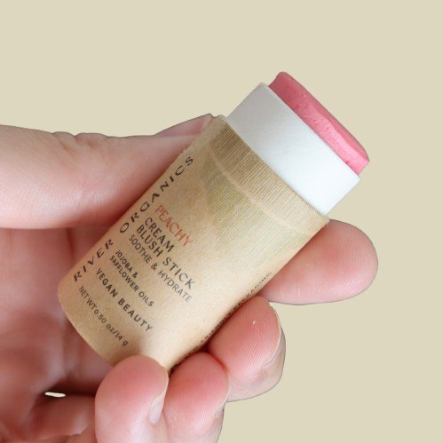 hand holding blush stick with cap off showing Peachy blush color