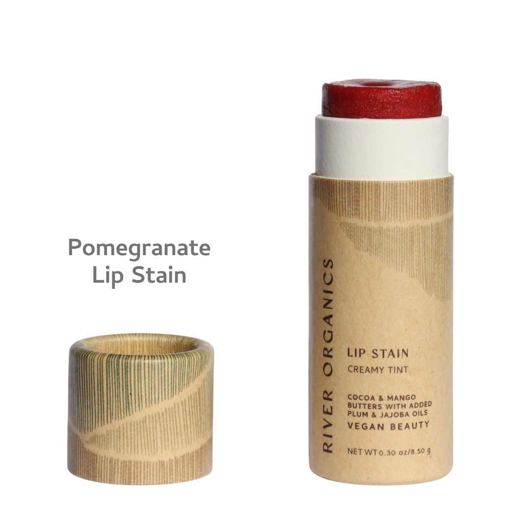 An open tube from the River Organics Lip + Concealer Set with its cap off reveals the vibrant red product inside. Text reads: “Lip + Concealer Set.” The tube is labeled as vegan and contains nourishing cocoa, mango, plum, and jojoba oils—perfect for anyone seeking a clean beauty routine.