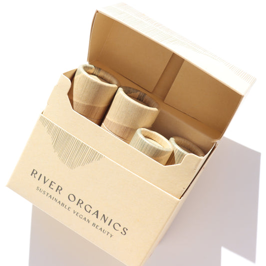 A cardboard box labeled "River Organics" holds four cylindrical bamboo containers, partially visible inside the open packaging—a Colour Sets natural makeup set ideal for eco-friendly beauty routines.
