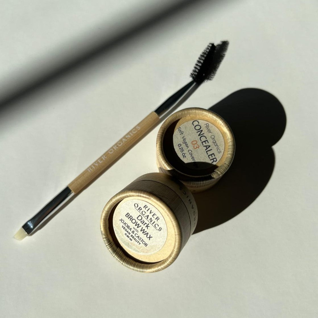 The River Organics Conceal & Brow Duo - Zero-Waste Vegan Beauty Set includes a dual-ended makeup brush and two small round containers for vegan concealer and brow wax, displayed on a light surface with soft shadows.