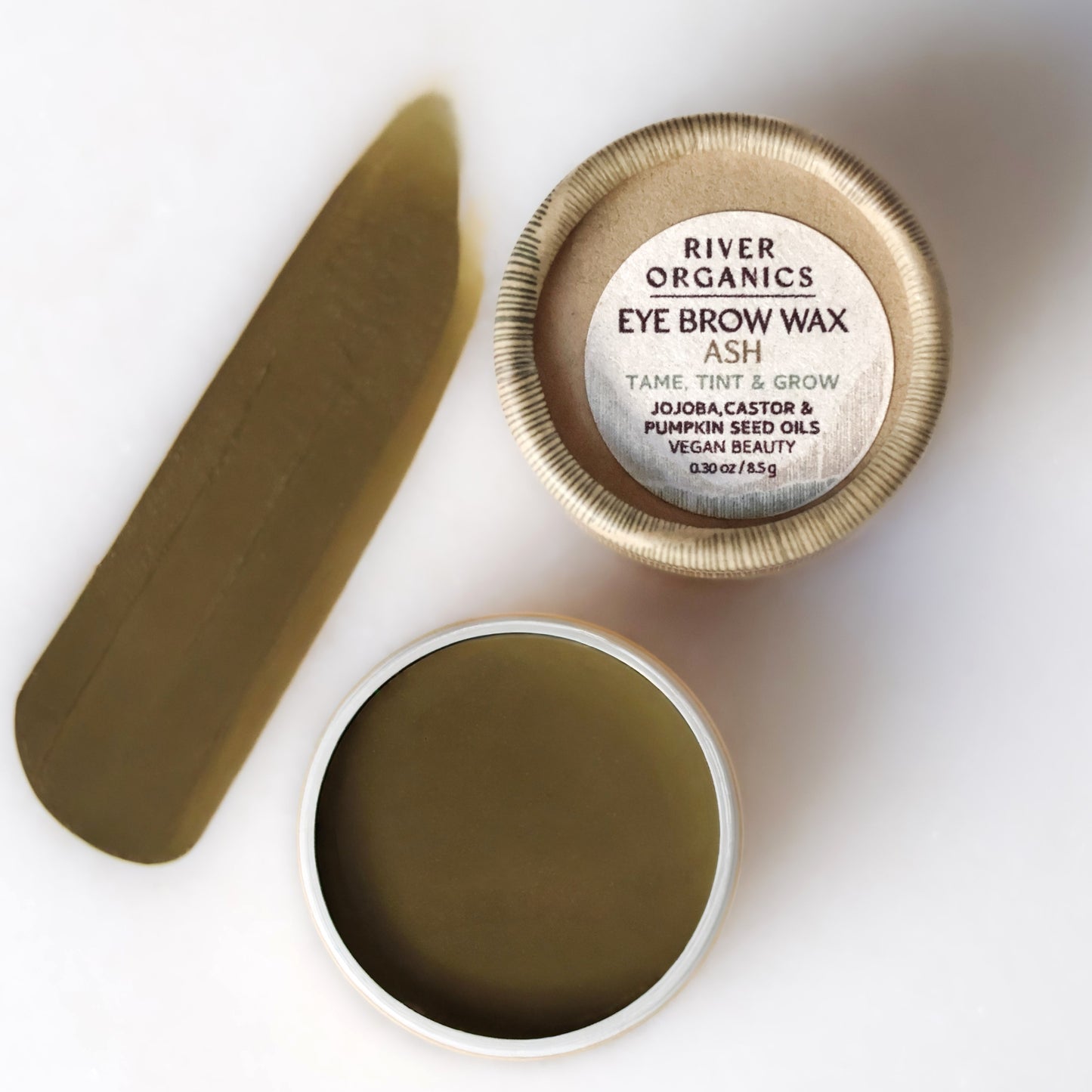 A round container of River Organics Brow Wax & Growth Serum sits open, displaying olive-green wax. Next to it is a swatch and the lid featuring product details. This vegan brow product offers both styling and growth benefits.