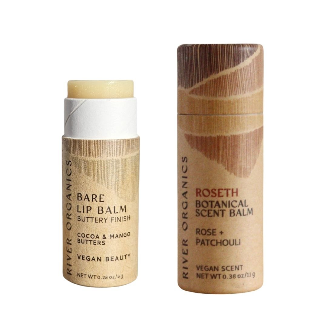 River Organics' Lip + Scent Balm Bundle features two cylindrical balms—one open, showing the off-white Vegan Lip Balm, and one closed Scent Balm—both in eco-friendly packaging with brown-toned labels for a botanical ritual.