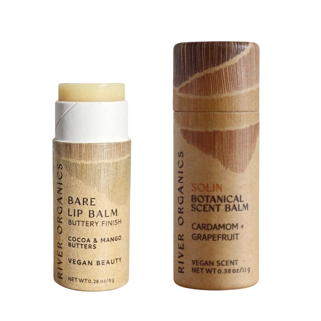 Two cylindrical cardboard tubes from River Organics’ Lip + Scent Balm Bundle—one open showing the Vegan Bare Lip Balm with cocoa and mango butters, one closed, the Solin Botanical Scent Balm—perfect for your daily botanical ritual.