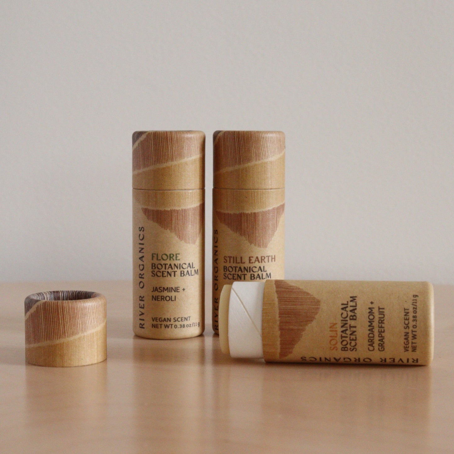A set of River Organics Botanical Scent Balms in brown, minimalist cardboard tubes sits on wood. One tube lies open, displaying the infused balm, while the remaining tubes stand upright. Available in sets of 2, 3, or 4.